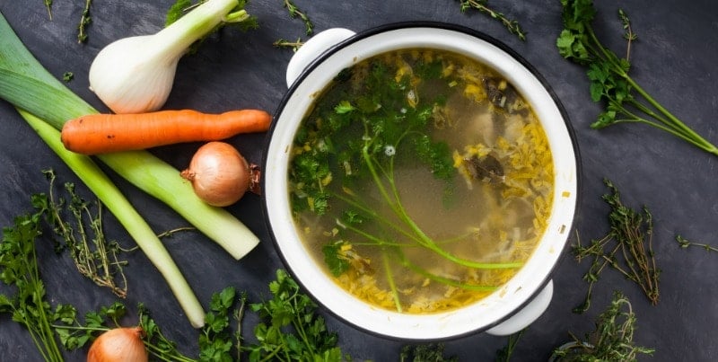 A pot of homemade stock surrounded by vegetables.