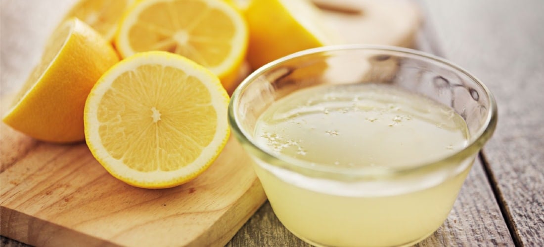 A bowl of lemon juice next to sliced fresh lemons