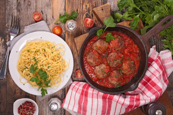 A frying pan with cooked meatballs next to a plate of spaghetti