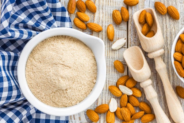 A top-down view of a bowl of almond flour next to almonds