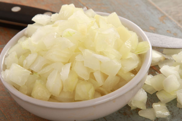 A bowl of diced onions next to a knife.