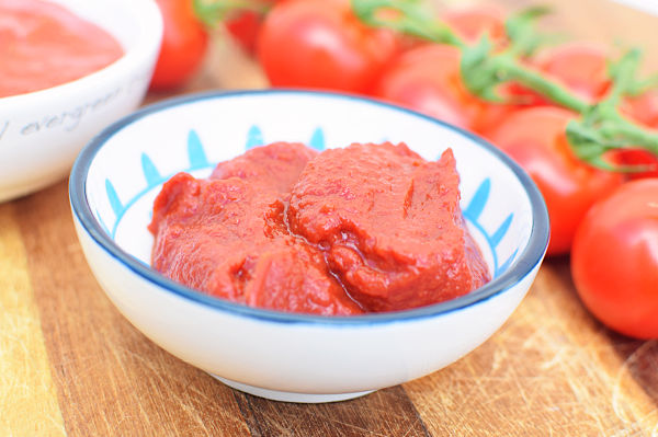 Tomato paste in a dish next to fresh vine-ripened tomatoes