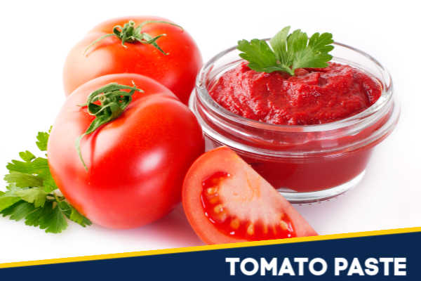 Tomato paste in a glass bowl next to fresh tomatoes.