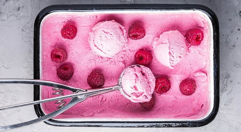 A container of raspberry ice cream scattered with fresh berries.