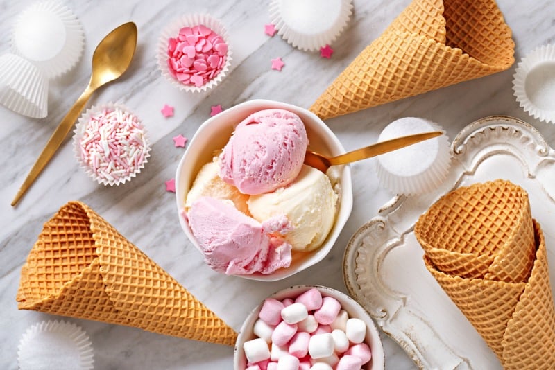 A bowl with scoops of strawberry and vanilla ice cream next to scattered cones.