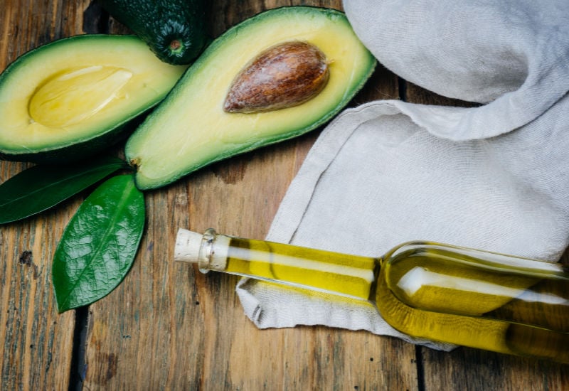 A bottle of avocado oil next to fresh avocados