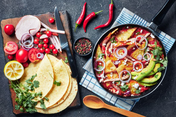 Chilaquiles verdes in a pan next to tortillas and vegetables