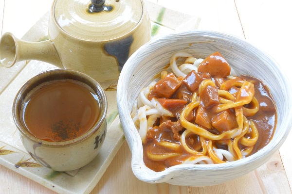 Curry udon next to a cup of tea