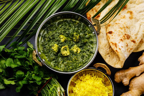 Vibrant palak paneer next to rice and naan bread