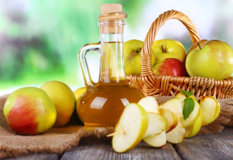 Apple cider vinegar in a jug next to apples
