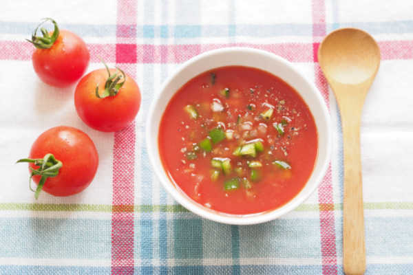 Gazpacho in a bowl next to fresh tomatoes