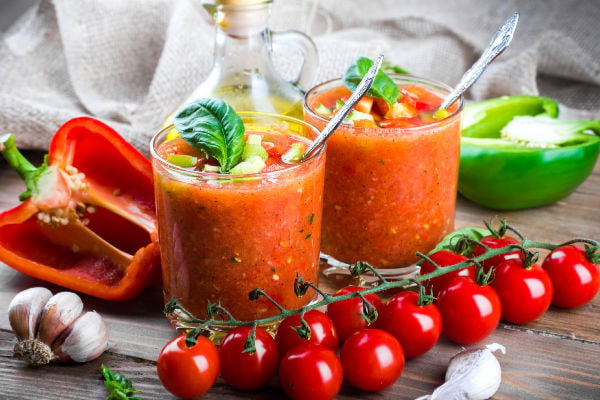 Two glasses of chilled gazpacho next to fresh tomatoes