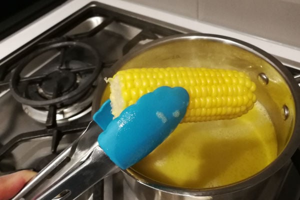 Tongs holding corn boiled in water and butter