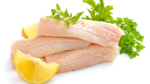 Fresh hake fillets next to lemon and herbs