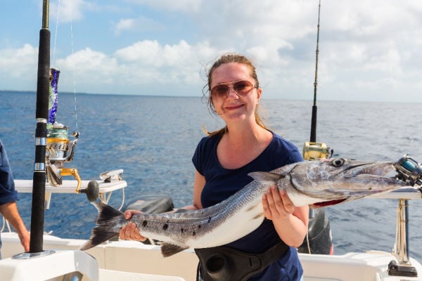 A woman holding a freshly caught barracuda on a boat