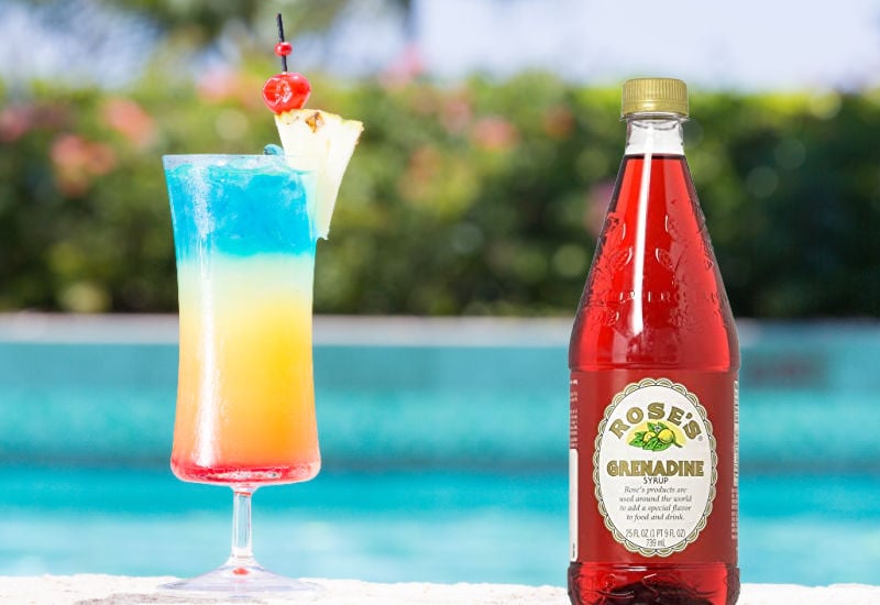 A cocktail next to a pool and a bottle of grenadine