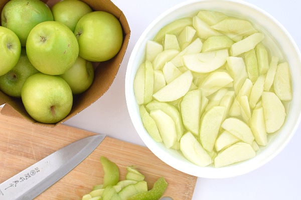 A bowl of apple slices in salted water and a bag of apples