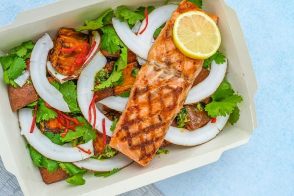 A salad topped with cooked salmon and a slice of lemon