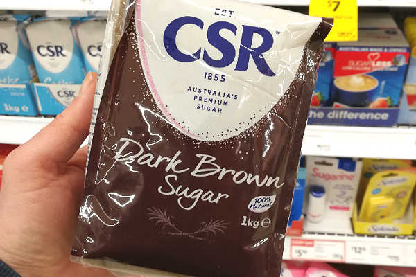 A bag of dark brown sugar with supermarket shelves in the background