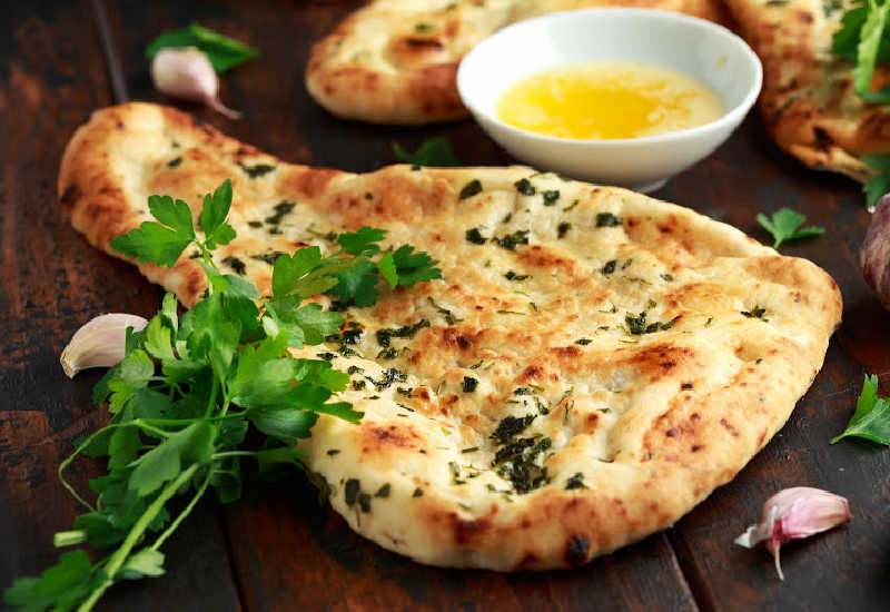 Naan bread on a table next to a bowl of oil