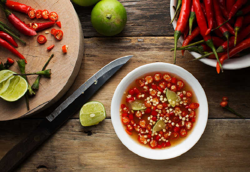 A bowl of nuoc mam next to fresh chili and lime