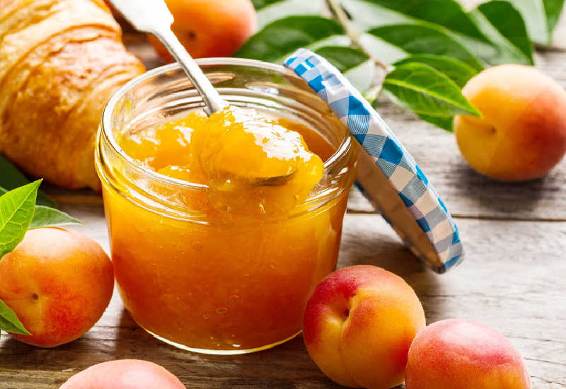 An opened jar of apricot jam next to fresh apricots