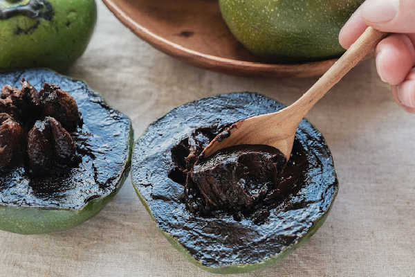 Scooping out ripe black sapote with a spoon
