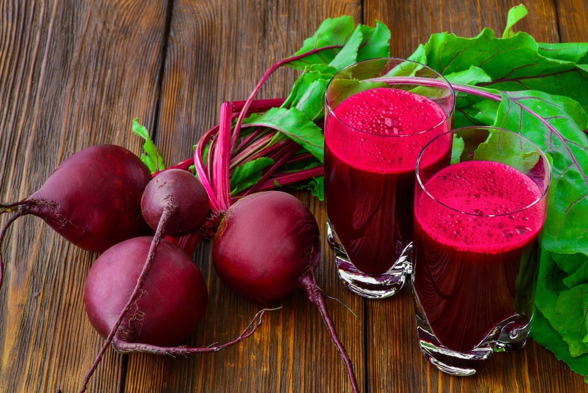 Glass of fresh beetroot juice with beets on wooden table