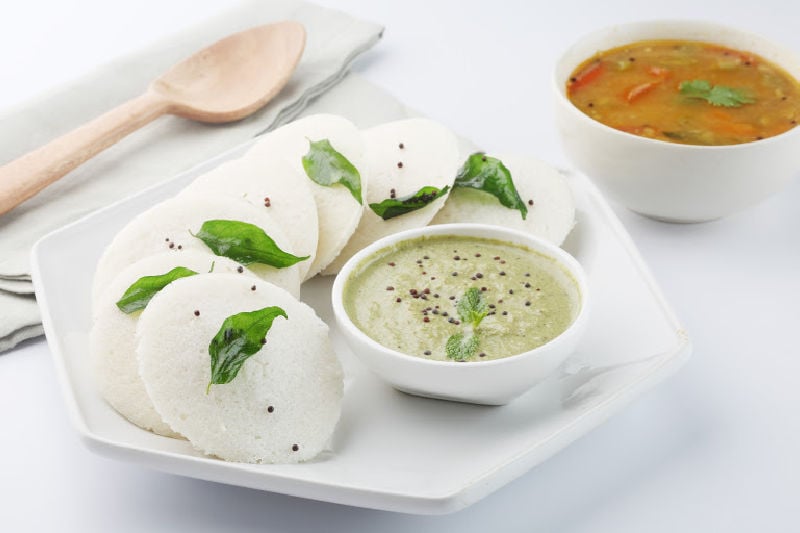 Idlis on a white plate next to a bowl of dipping sauce