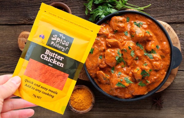 Holding a butter chicken spice sachet next to a pot of butter chicken