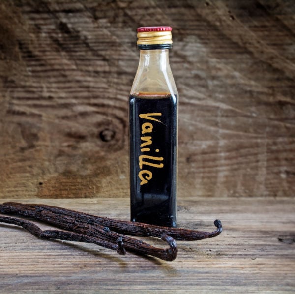 Bottle of homemade vanilla extract next to vanilla beans