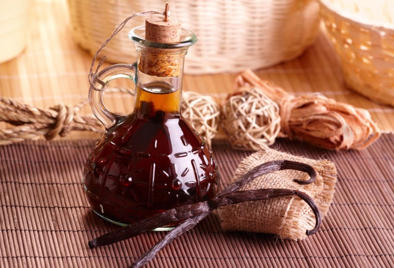 Homemade vanilla extract in a bottle next to vanilla beans