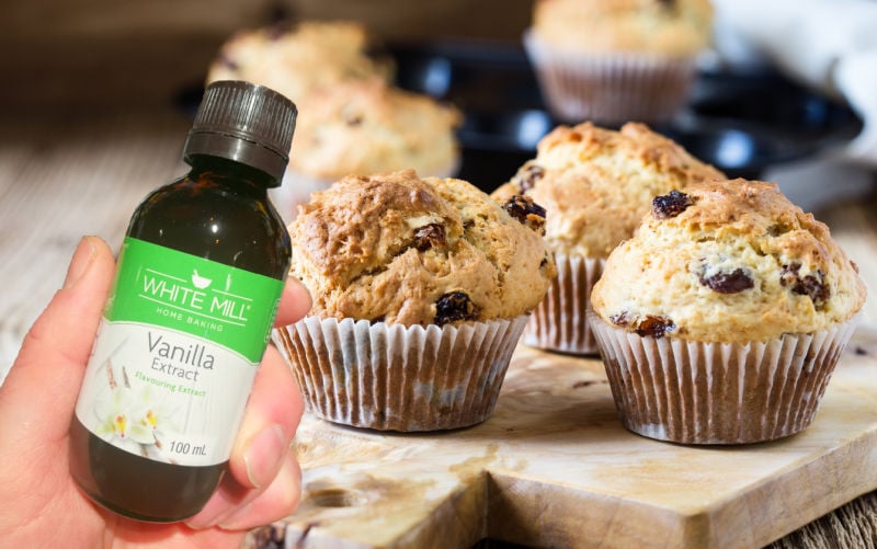 Holding a bottle of vanilla next to baked muffins