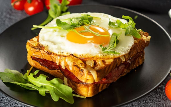 Croque Madame on a black plate with arugula garnish