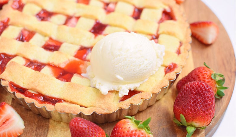 Baked strawberry crostata surrounded by strawberries and a scoop of vanilla ice cream