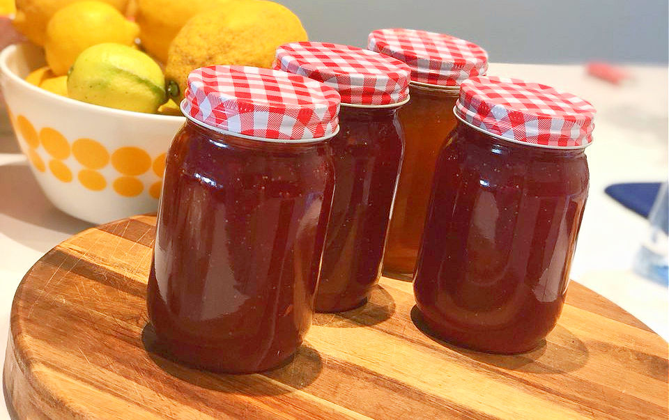 Homemade strawberry jam in jars with a bowl of lemons in background