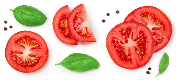 Sliced tomatoes next to basil leaves