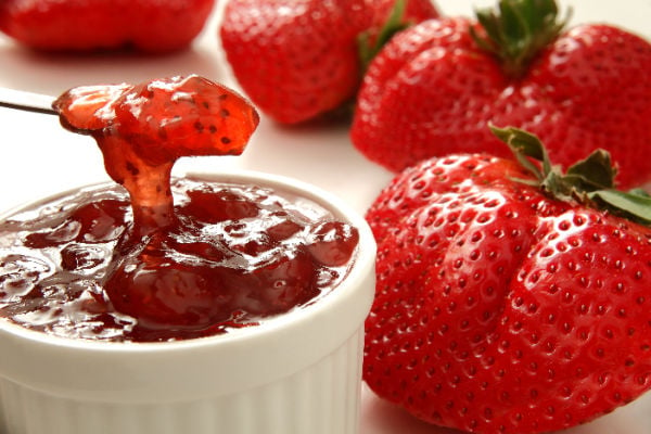 Fresh strawberry jam in a bowl next to strawberries