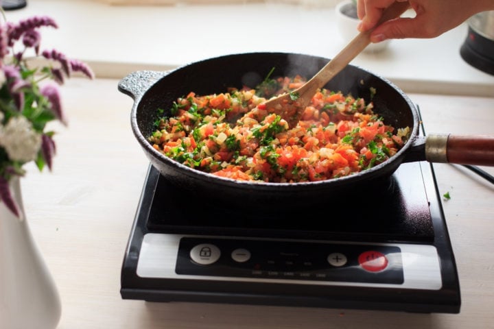 Induction cooking at home on a black portable cooker in cast iron cookware