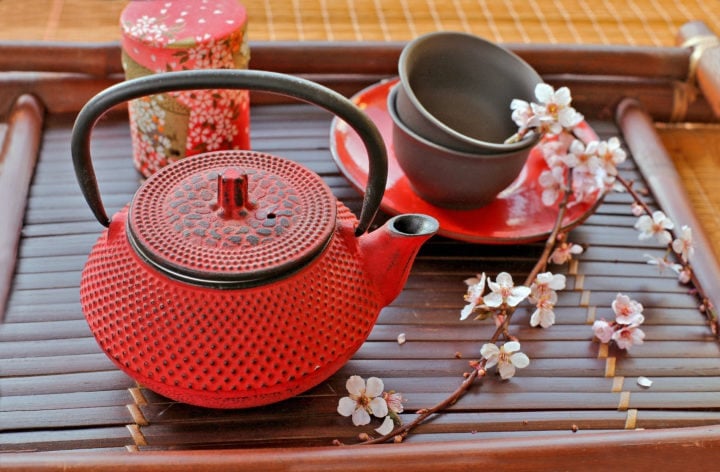Cast Iron tea pot with cups and blossom pink flowers on bamboo tray