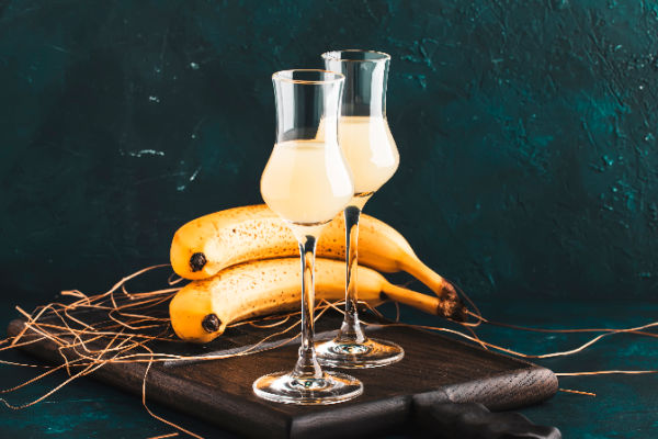 Two glasses of Homemade Banana Liqueur Recipe next to fresh bananas