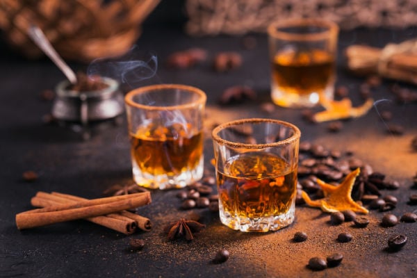 Spiced whiskey next to cinnamon sticks and other spices