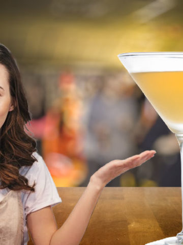 A Yellow Submarine cocktail on a bar counter next to a lady in an apron