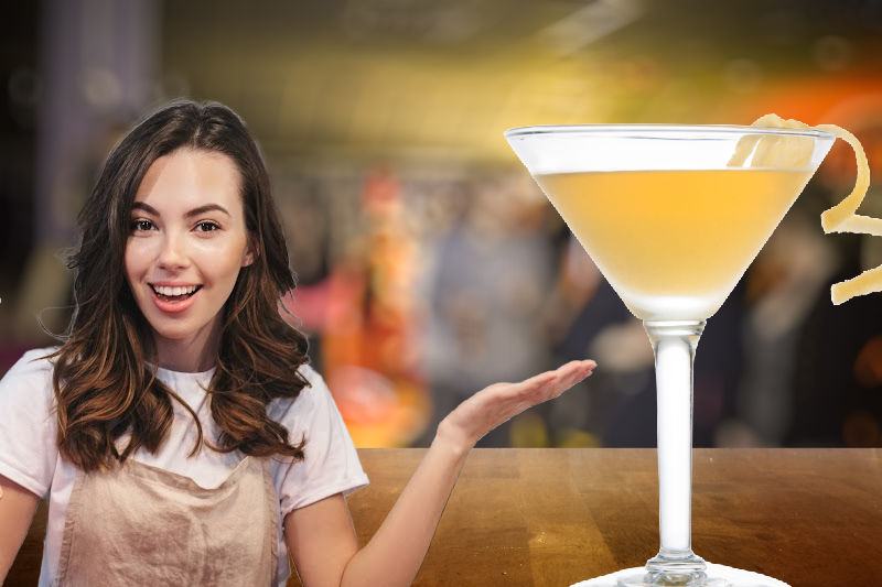 A Yellow Submarine cocktail on a bar counter next to a lady in an apron