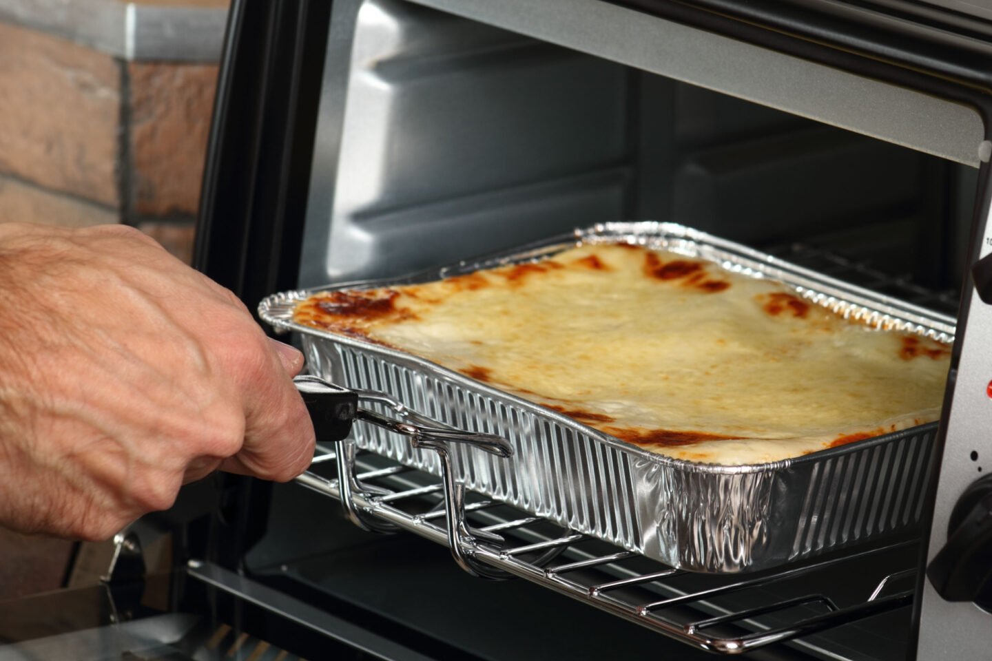 man putting lasagna in aluminum dish into electric oven