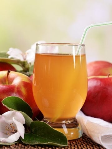 a glass of fresh apple juice together with red apples