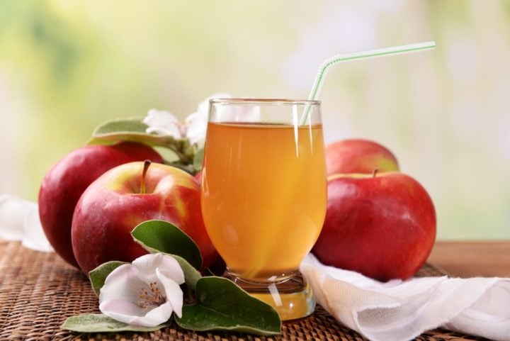 a glass of fresh apple juice with straw surrounded with red apples
