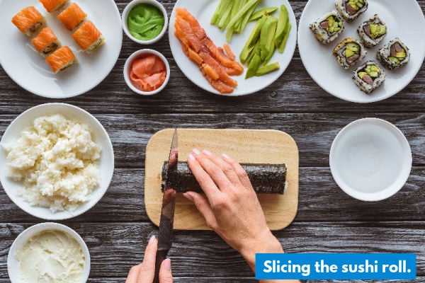 A lady slicing up a sushi roll