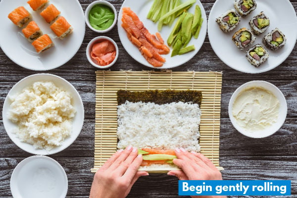 Two hands beginning to roll sushi on a mat