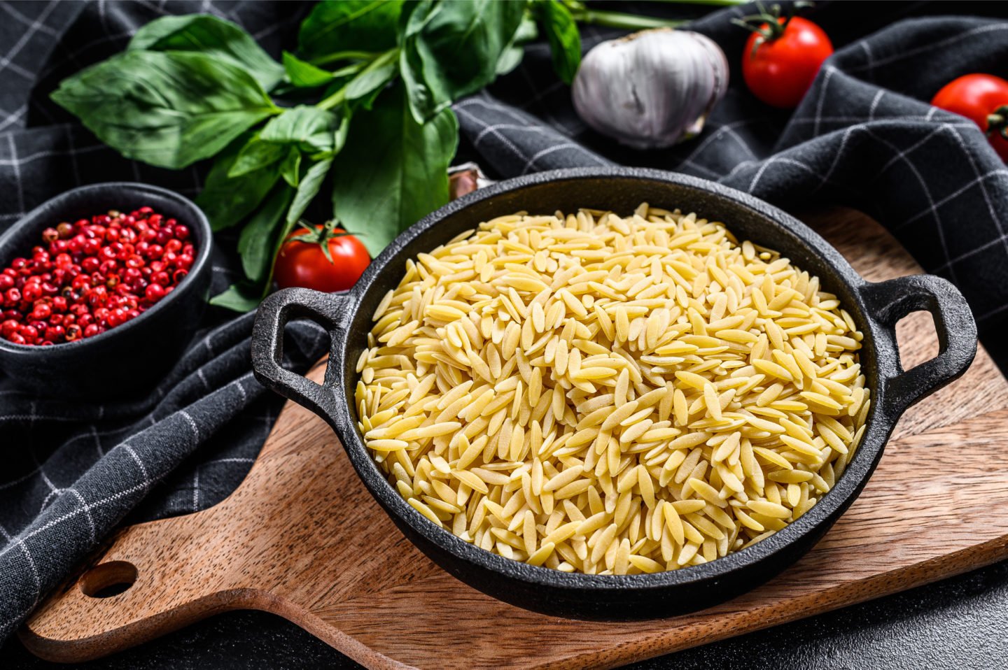 uncooked orzo in casserole with tomatoes and garlic in background